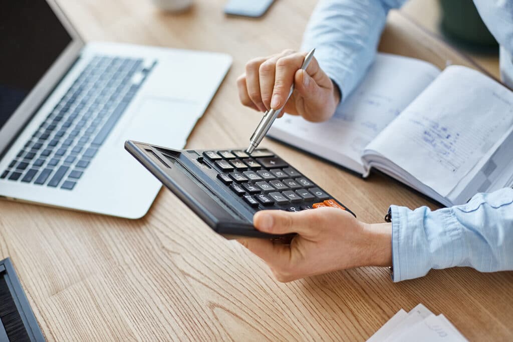 Mains utilisant une calculatrice à côté d’un ordinateur portable et d’un carnet
